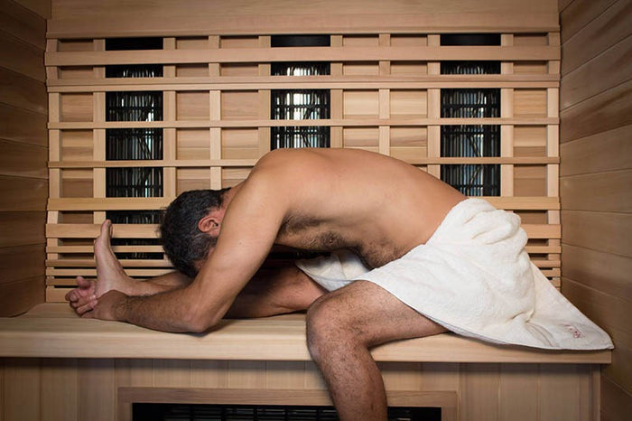 Man lying on a wooden bench in a sauna with a towel wrapped around him.